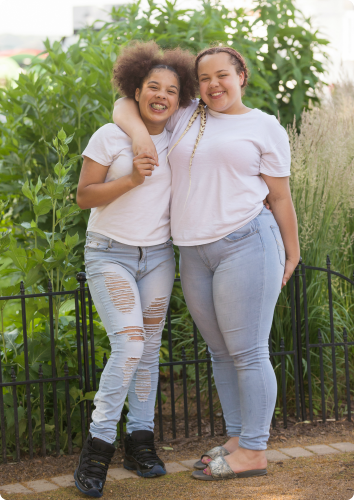 Paige and Gabby smile big with their arms wrapped around each other's shoulders. They wait to be adopted.