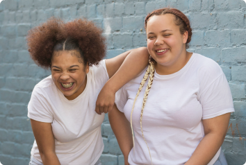 Paige and Gabby, in matching outfits, laugh in front of a blue brick wall. They wait to be adopted from foster care.