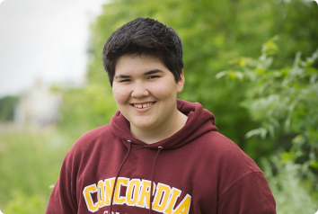 Genesis, a social teen in foster care, smiles wearing a maroon sweatshirt in a green field.