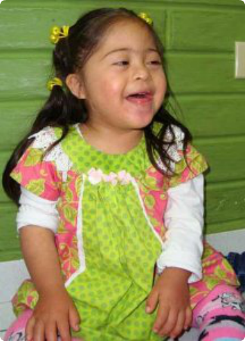 A five year old girl waiting for adoption smiles in a bright green dress. 