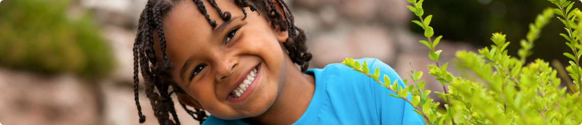 A school-aged African American boy in foster care smiles with braided hair.