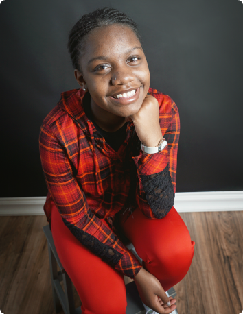 Jahnia, a teen in foster care, smiles brightly in a red plaid shirt.