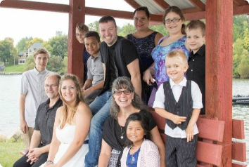 The entire family, many of whom were adopted from foster care, smile in front of a lake.