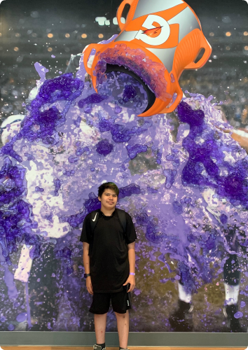 Jose, a teen waiting in foster care, smiles in front of a gatorade all mural at the Vikings training facility.