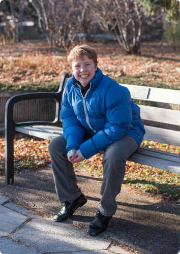 A picture of Sean smiling on a park bench. He waits in foster care for an adoptive family.