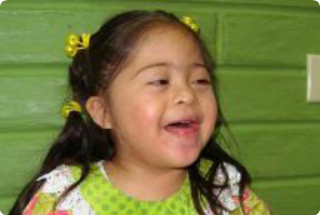 A five year old girl waiting for adoption smiles in a bright green dress.