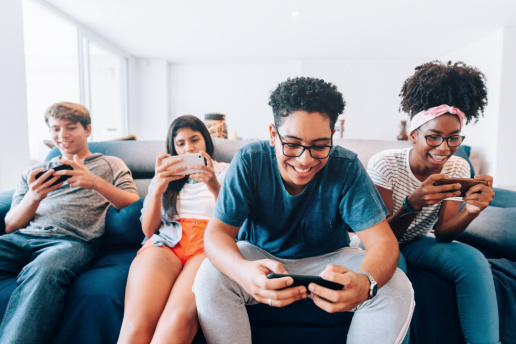 Four diverse teens sit on couch playing games on phones