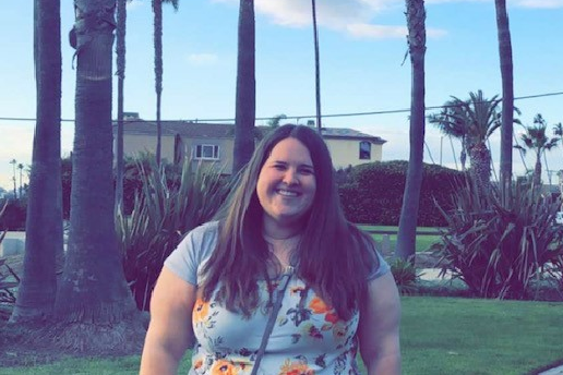 Woman smiles in front of palm trees in floral t-shirt