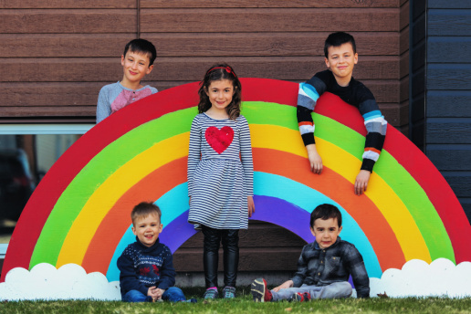 Five siblings pose around a cutout rainbow