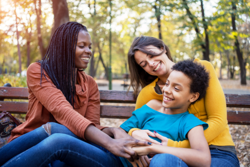 LGBTQ Family smiles outside on park bench