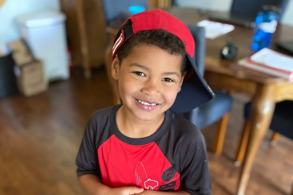 boy smiles wearing red baseball cap sideways