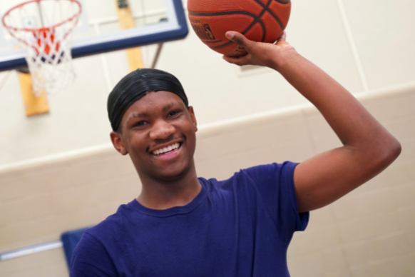 African American teen smiles while playing basketball