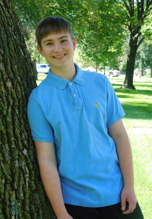 Teen boy smiles outside leaning against tree