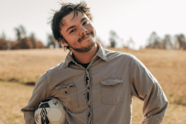 Colby, a 17-year-old waiting for his forever home, holding a soccer ball in a grassy field