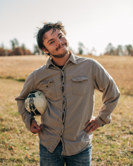 Colby, a 17-year-old waiting for his forever home, holding a soccer ball in a grassy field