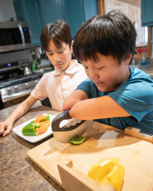Jiangli using adaptive cooking equipment to chop peppers with his brother in their kitchen