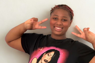 Ari giving two peace signs and wearing a tshirt with Aaliyah on it
