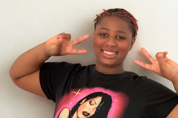 Ari giving two peace signs and wearing a tshirt with Aaliyah on it