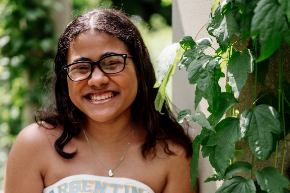 Trinity smiling next to an ivy covered wall on a sunny day