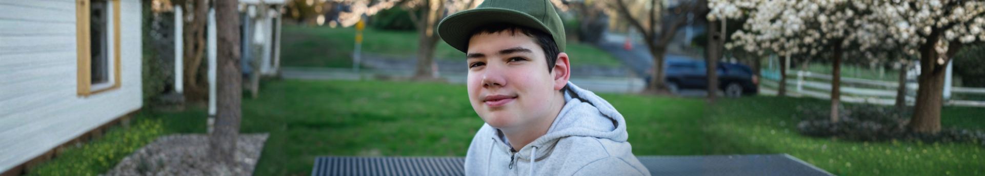 boy wearing a hat and hoodie sitting at a picnic table on a summer evening