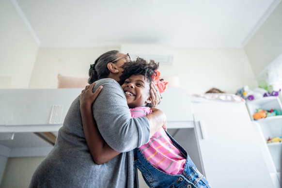 Grandmother and granddaughter hugging and smiling at each other on a couch.