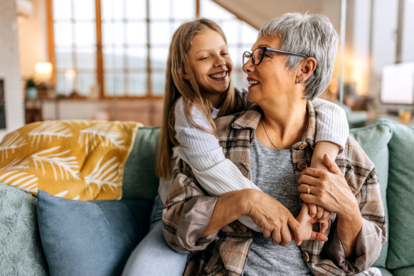 Grandmother and granddaughter smiling at each other on a couch.
