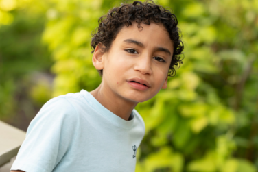 portrait of JJ in front of green leaves on a sunny summer day