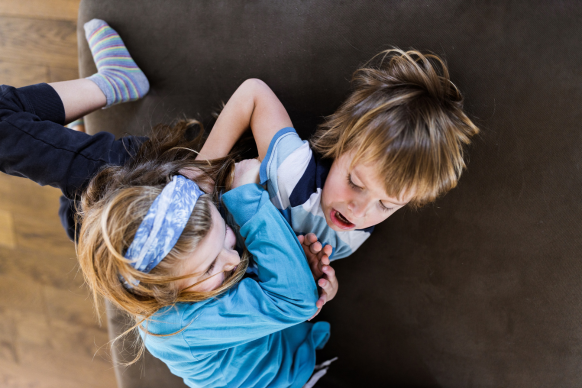 a young boy and a young girl wrestling on a couch